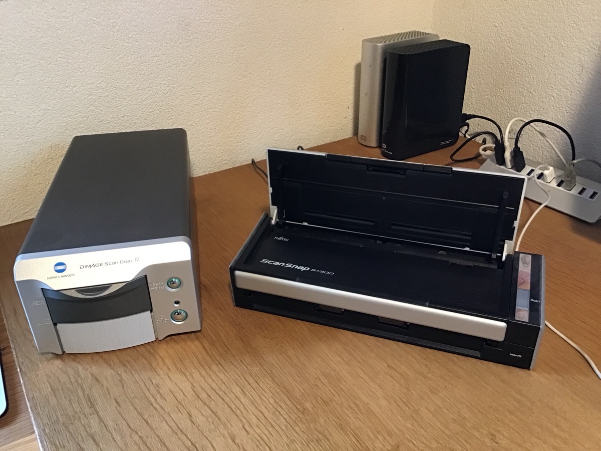 Un scanner à film Minolta et un scanner à documents Fujitsu côte à côte sur une table en bois. Au fond on devine deux disques durs externes et un multiprise USB.