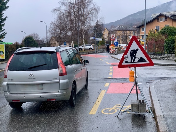 Panneau annonçant des travaux posé sur une bande cyclable et empêchant le cycliste d'avancer, en raison d'une autombile passant au même moment à sa gauche.